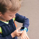 Wearable kids baby smart watch calls mom and location tracking with touch screen and voice service, blue multicolored electronic gadget with rubber wristband for children. Close up boy with copy space. Time clock for school.
