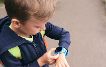 Wearable kids baby smart watch calls mom and location tracking with touch screen and voice service, blue multicolored electronic gadget with rubber wristband for children. Close up boy with copy space. Time clock for school.